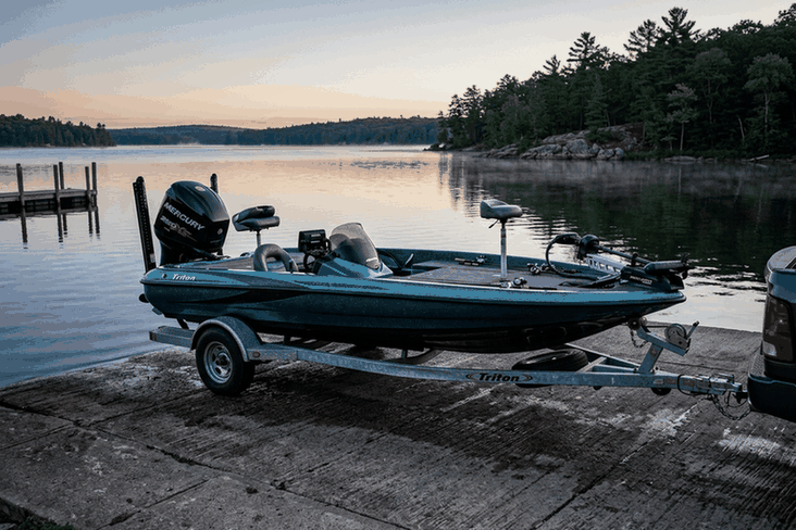 Bass boat with a large outboard on its trailer at a boat ramp