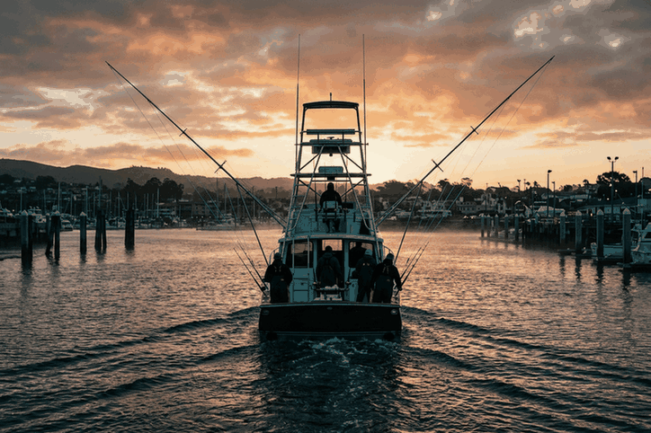 Charter fishing boat with anglers leaving the harbor at sunrise