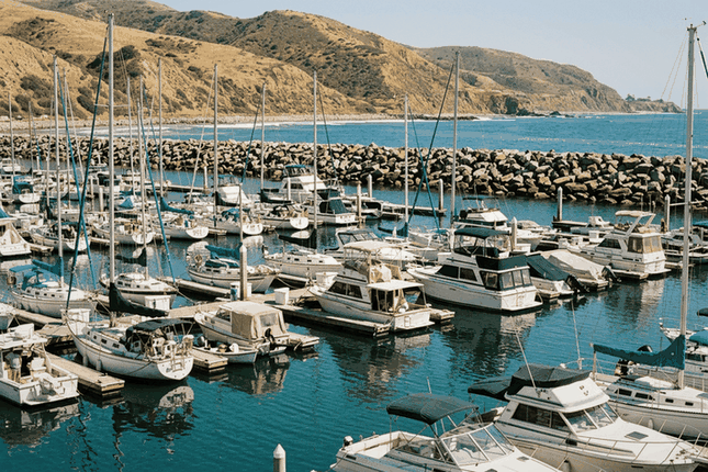 Sailboats and motor yachts at a California marina below dry golden hills, as kept by many California boat owners