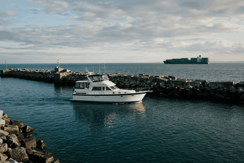 Motor yacht leaving a harbor with a cargo ship offshore, the two sides of marine insurance